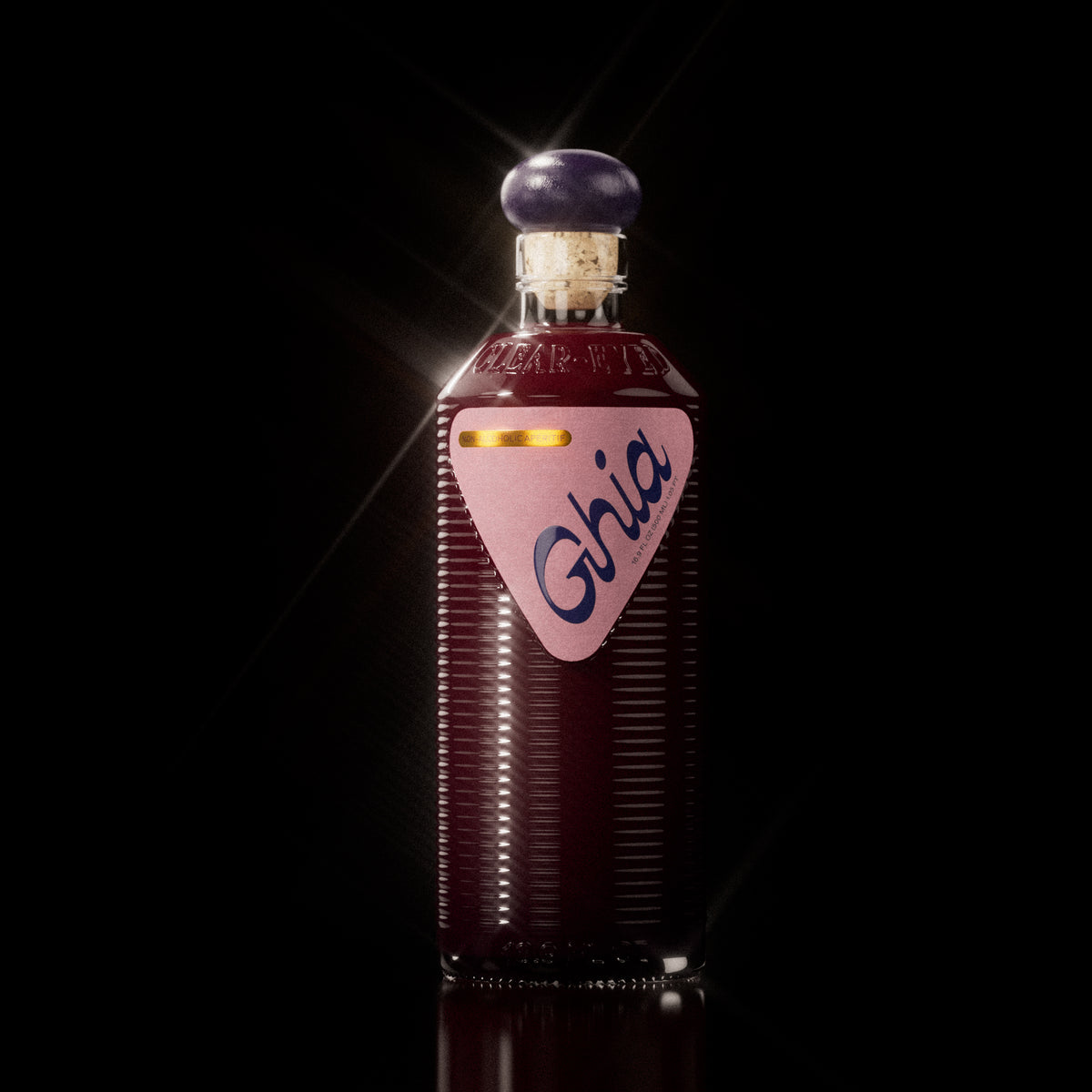 A Ghia non-alcoholic beverage in flavor Berry Apéritif clear bottle with ribbed glass, a purple cork top, and a pink label featuring bold branding on a reflective surface.