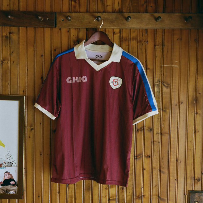Maroon Ghia Jersey on a wooden hanger against a knotty pine wall